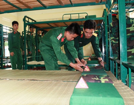 Trong những ngày đầu quân ngũ, các chàng “tân binh” được hướng dẫn các nội dung ngoại khóa, làm quen với 11 chế độ trong ngày, 3 chế độ trong tuần để chuẩn bị bước vào khóa huấn luyện chính thức. Trong ảnh là sĩ quan chỉ huy giúp chiến sĩ mới gấp chăn màn vuông vức.